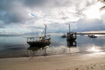 Wooden sailboats on the water at the beach at sunrise in Mafia Island, Tanzania, with cloudy sky and calm water.