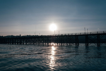 Fototapeta premium Silhouette of wooden and long bridge over the river (Mon Bridge) in the evening 