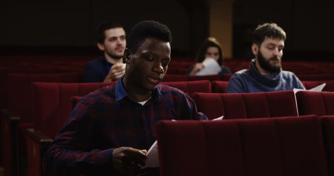 Medium shot of actors memorizing their lines while sitting in the auditorium