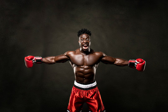 Muscular African American Black male sweaty boxer does an aggressive scream with arms open looking at camera with dramatic lighting with a black background  