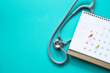 Top view of stethoscope and calendar on the green background, schedule to check up healthy concept