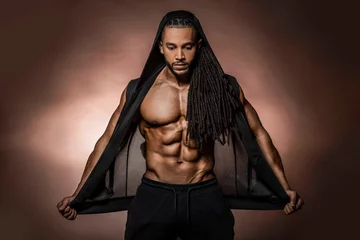 Muskulöses afroamerikanisches schwarzes athletisches Fitnessmodell mit schwarzem Hoodie mit Sixpack-Bauchmuskeln im Studio mit dramatischer Beleuchtung vor braunem Hintergrund © Paul