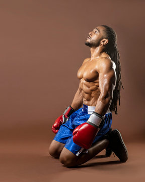 Muscular African American Black Male Sweaty Boxer On Knees,  Knocked Down Trying To Get Up With Dramatic Lighting With A Brown Background  