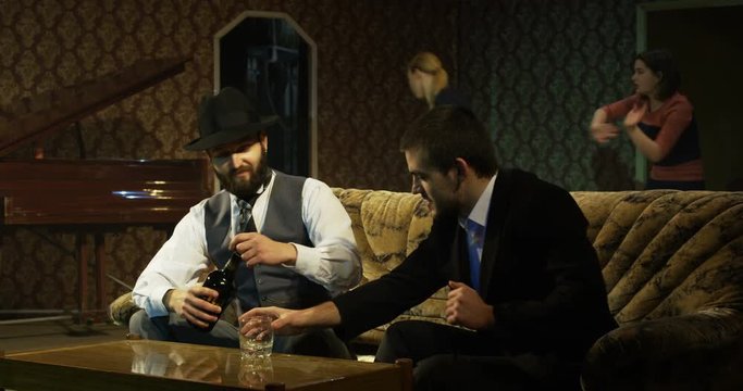 Medium Shot Of Male Actors Drinking While Sitting On A Sofa While Actresses Performing A Tense Scene In The Background