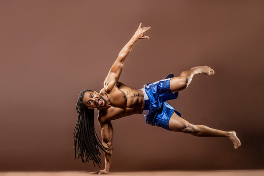 Muscular African American Black athletic man with long dreadlocks hair does a hand balance exercise in studio with dramatic lighting with a brown background  