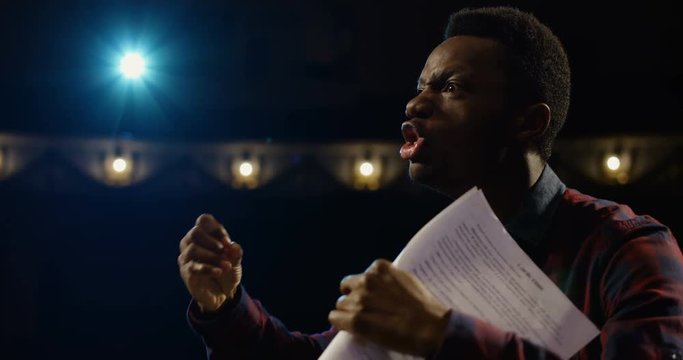 Medium close-up shot of an actor performing a monologue in a theater while holding his script