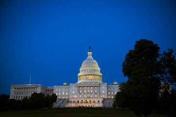 Scenic evening view of the US Capitol Building with glowing lights under blue dusk sky in...