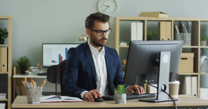 Portrait shot of the handsome official worker man typing on the keyboard of the computer in the nice cabinet room.