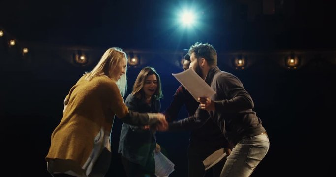 Medium shot of actors and actresses throwing scripts away and hugging while celebrating on stage in a theater