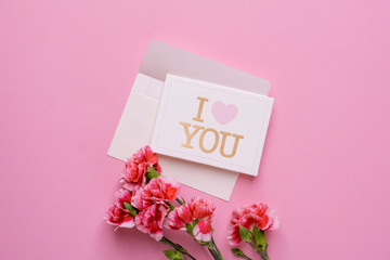 An envelope with card I love you and pink flowers on a pink background