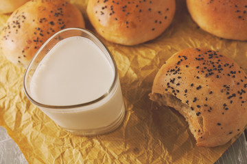 Freshly baked burger buns with black sesame on a baking paper. Fresh from the oven. glass of milk