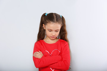 Sad abandoned kid girl in red Christmas blouse looking unhappy with folded arms looking down
