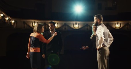 Medium shot of actors rehearsing in a theater while reading their scripts