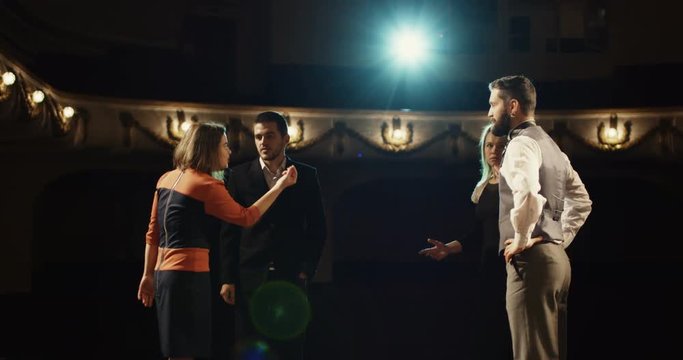 Medium shot of actors rehearsing in a theater while reading their scripts