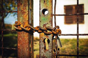 Rusty iron chain on the gate with big lock in front of the house - image