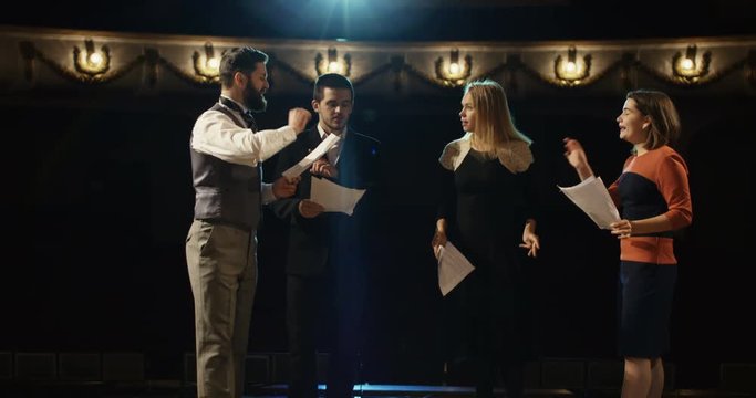 Medium shot of actors rehearsing in a theater while reading their scripts
