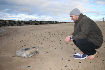 Close up of man and seal, friendly Winter rescue encounter on beach with baby grey seal pup and man looking towards each other on sandy beach near shore rocks background in Norfolk East Anglia England