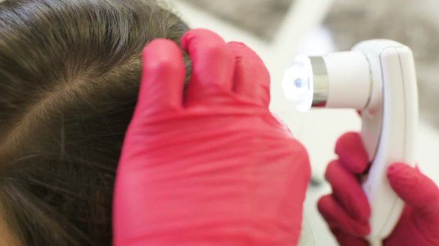 doctor dermatologist diagnoses the structure of the hair of a young pretty girl with a special tool - a trichoscope. Trichology, trichogram