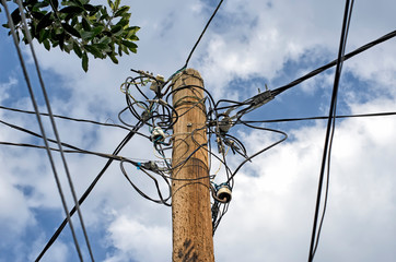 A pole with insulators and a multitude of electrical cables against a cloudy sky.