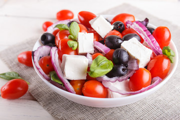 Greek salad with fresh cherry tomatoes, feta cheese, black olives, basil and onion on white wooden...