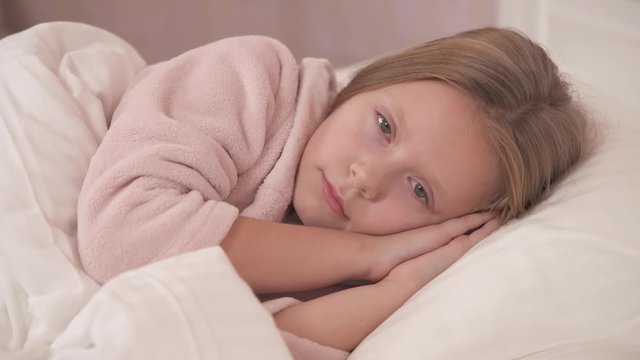A close-up of girl's face lying sidelong and sleeping in bed. The girl opens her eyes and smiles a bit