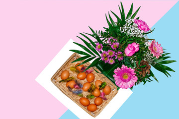 Bouquer of flowers and basket with eggs and feathers on blue pink background.