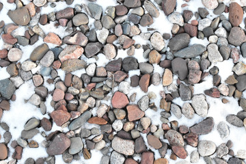 River rock stones in grey and red as garden mulch covered in light snow in winter