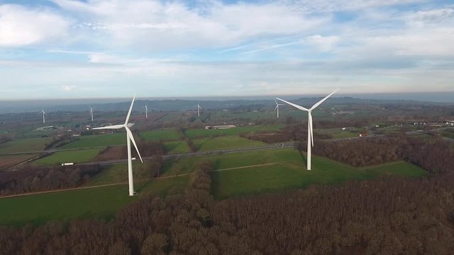 Wind turbines along a highway and fields in Normandy France. Drone aerial back track early morning.