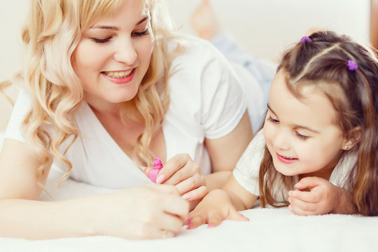 Happy Mother and child daughter in hair curlers paint nails, make a pedicure