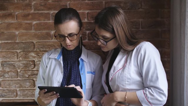 Woman doctor and girl Intern discuss a patient's diagnosis depends on the history on the tablet.