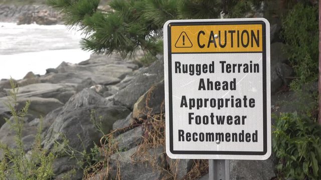 Rugged Terrain caution sign along ocean rocks 4k
