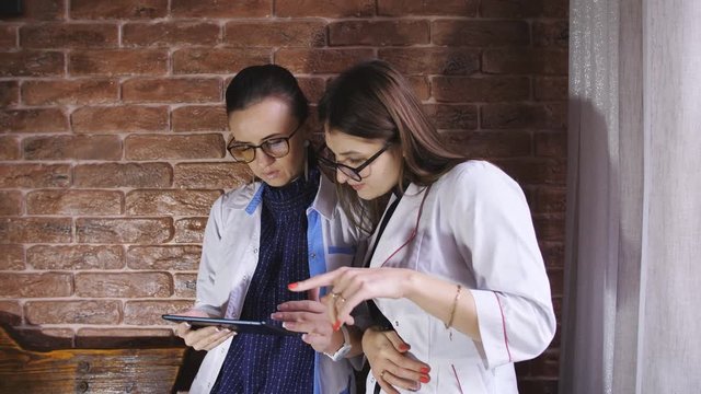 Woman doctor and girl Intern discuss a patient's diagnosis depends on the history on the tablet.