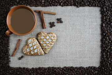 Filiżanka kawy otoczona ziarnami kawy, obok cynamon i piernikowe serca