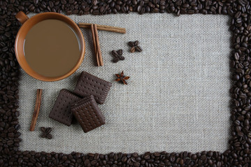 Filiżanka kawy  otoczona ziarnami kawy, obok cynamon i czekoladowe ciastka
