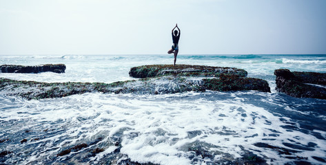 Young woman practice yoga at the seaside coral cliff edge