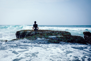 Yoga woman meditation at the seaside coral cliff edge facing the sea waves