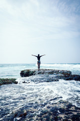 Cheering woman outstretched arms at seaside mossy coral reef