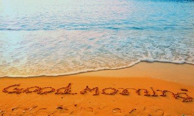 The word of good morning writing on sand beach with waves blue ocean.