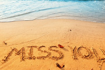 Valentine's day concept, miss you writing on sand beach with waves blue ocean.