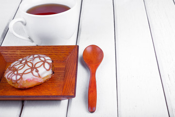 A cup of tea and sweet donut on wooden plate over  wooden tabletop with wooden  spoon. Celebration concept