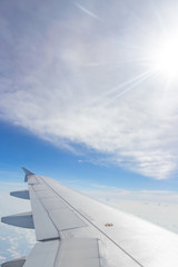 Fototapeta na wymiar Airplane Wing & Blue sky with clouds Sky View from Airplane Window while Sun is shining through