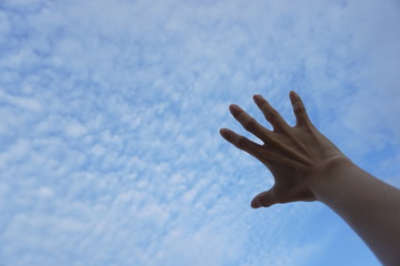 Hand reaching to towards blue sky and clouds. Hand on the sky background.