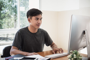 Attractive Asian businessman / student young man sitting working busy for seaching information data internet at office technology center room near document report on desk