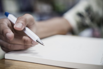 Man student taking and writing notes on notebook with pen in library at college university for...