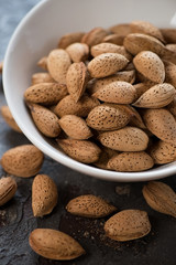 Close-up of unpeeled almond nuts in a white bowl, selective focus