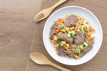top view of fried rice with beef in a ceramic dish on wooden table. asian homemade style food concept.