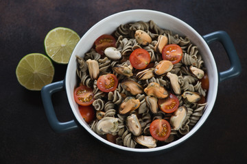 Bowl of hemp flour fusilli served with mussels and cherry tomatoes, horizontal shot on a dark brown metal background