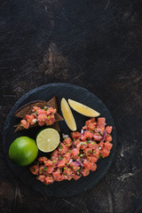 Stone slate with salmon tartar on a dark brown stone background, vertical shot with space, top view