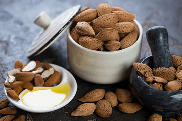 Bowl of unpeeled almonds and freshly made almond oil, selective focus, closeup
