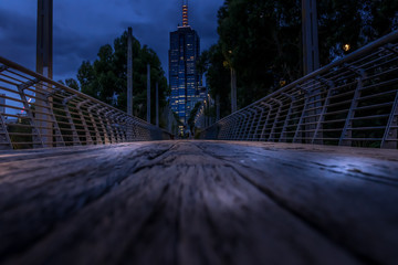 Wooden pedestrian bridge at night, with city scape in the background.